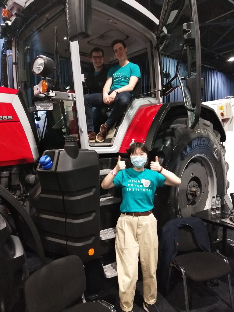 Photo of Dan, Dan and Xinyun posing sat in side and stood in front of a tractor with their thumps up.